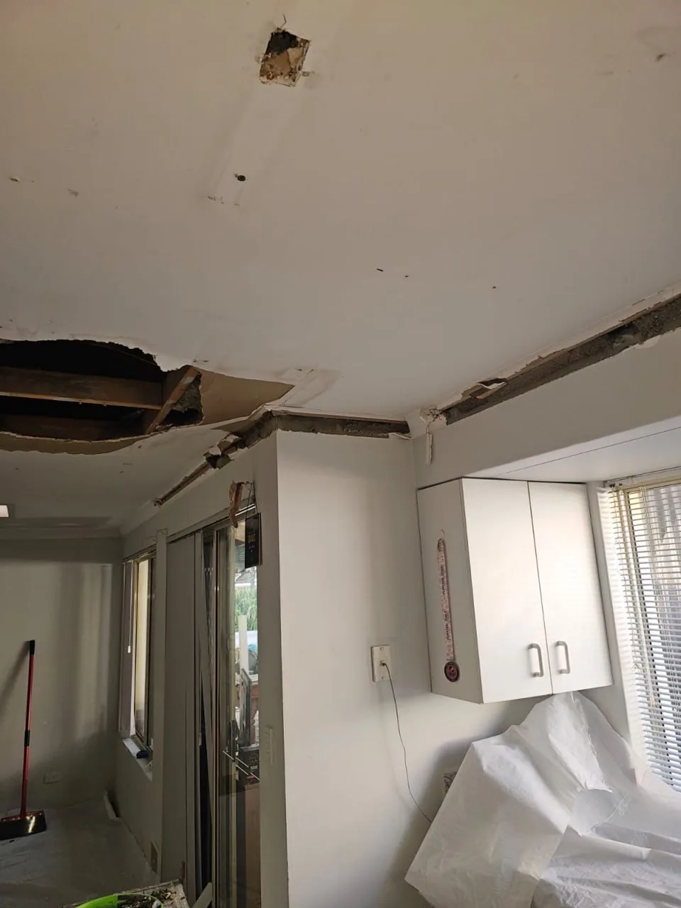 Kitchen ceiling in a Bassendean home torn back to the bare timber joists, with the plaster cornice broken away around the perimeter and plastic sheeting draped over the benches below