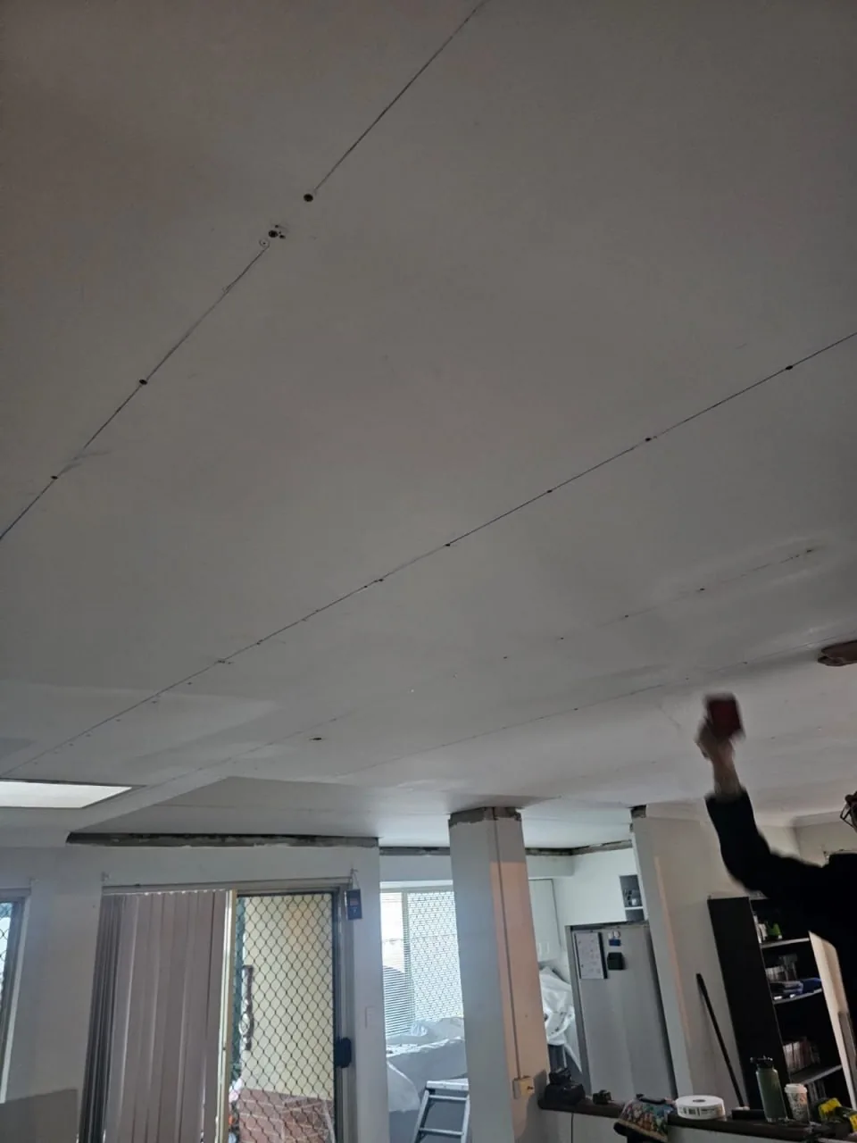 A crew member reaching up with a sanding block to a Bassendean living area ceiling where a screw line has been patched and the cornice has been stripped back