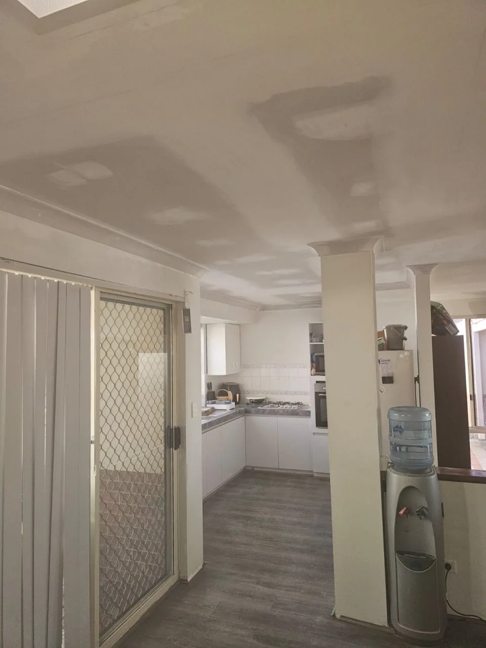 The same Bassendean kitchen doorway with the ceiling replaced, set flat and sanded, the cornice refitted along the wall and around the column, and the room back in use