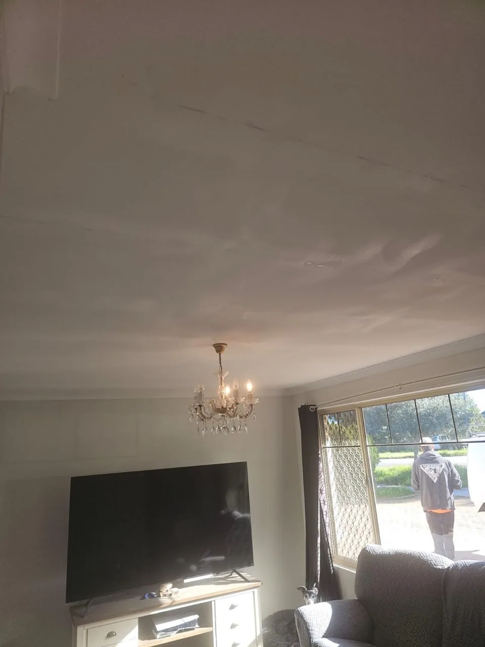 Lounge ceiling in a Bassendean home with the cracked join patched and sanded flat, seen from below the chandelier