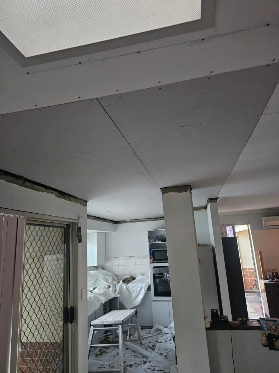 New plasterboard sheets screwed up across a Bassendean kitchen ceiling with the joins not yet flushed, a step ladder underneath and debris still on the floor