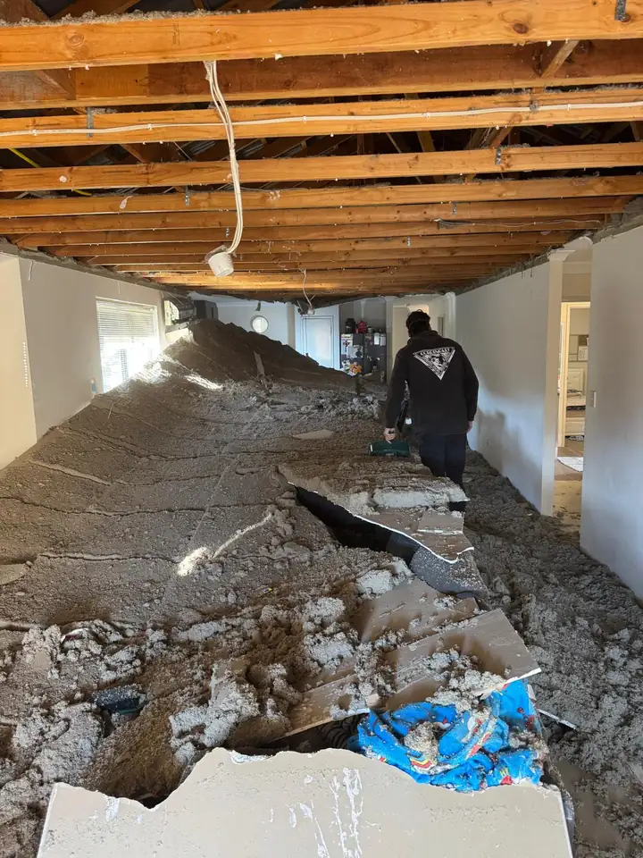 A crew member walking through an Ellenbrook living room clearing collapsed ceiling debris and insulation piled waist high