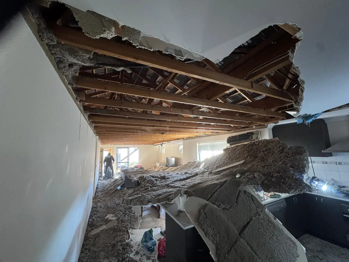 Collapsed ceiling seen from the kitchen end of an Ellenbrook home, with insulation across the benchtops and exposed roof battens overhead