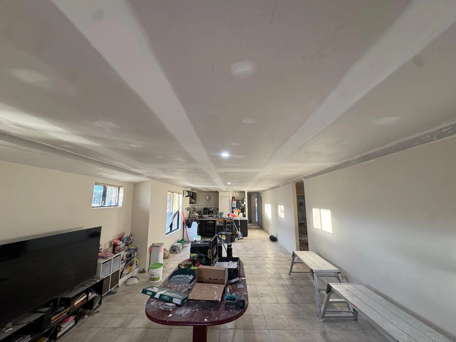 The same Ellenbrook lounge and kitchen after replacement, with the new ceiling sheeted and flushed ready for paint