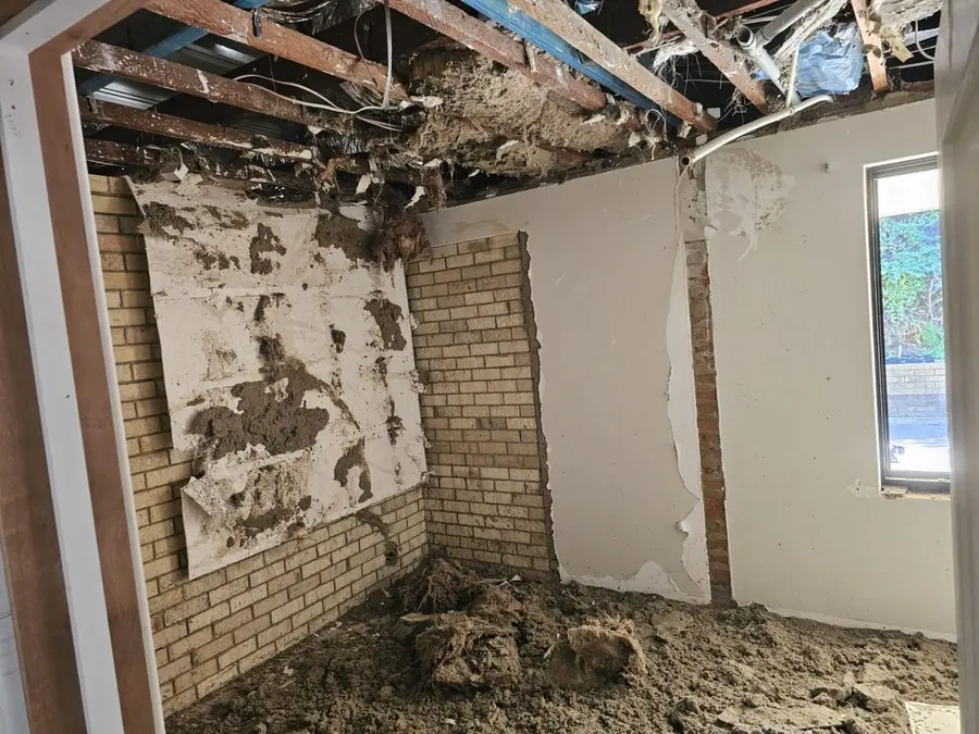 A Roleystone room during the ceiling strip-out, with debris heaped across the floor, the brick wall stripped back to bare and the old wall lining torn away