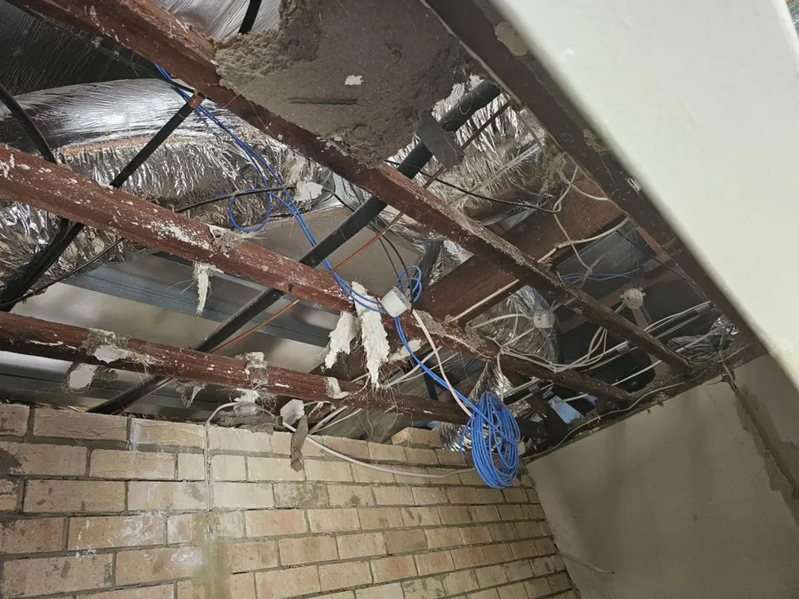 Looking up at the exposed roof timbers and battens of a Roleystone house with the ceiling completely removed, brick walls bare on either side