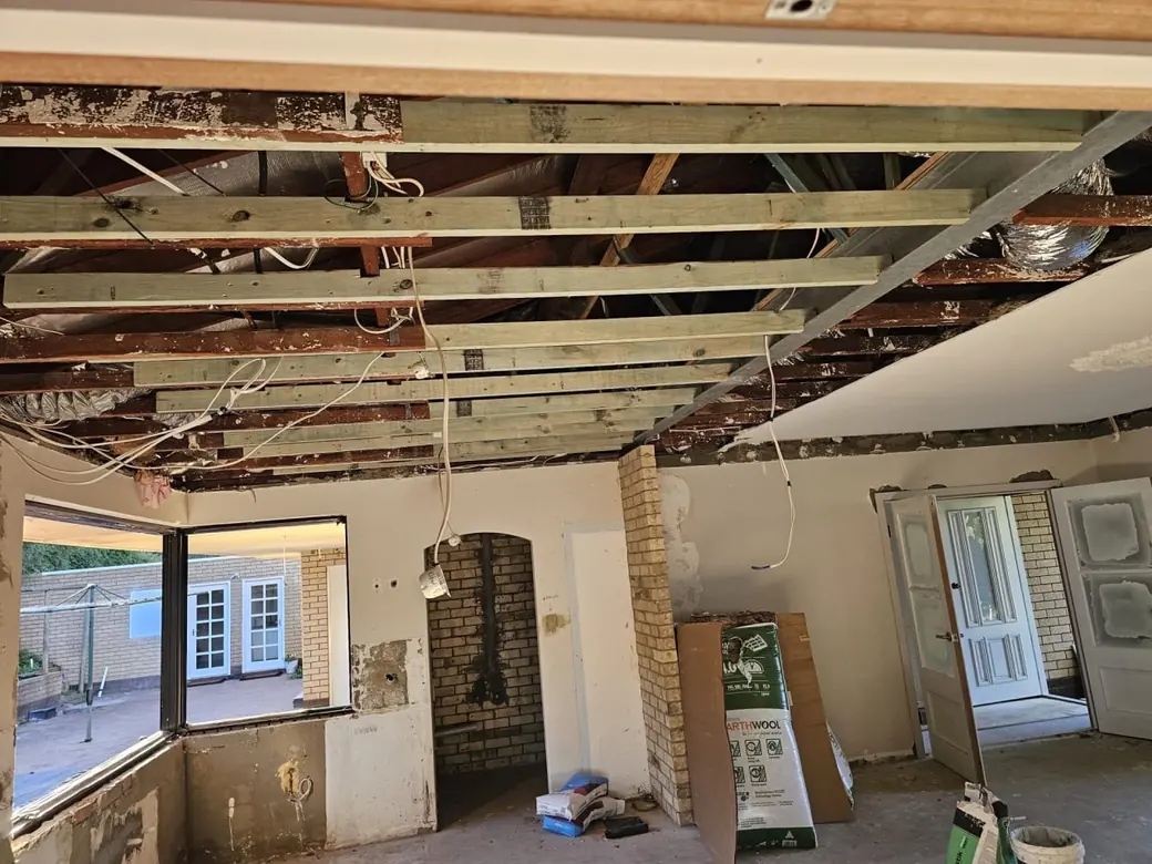 The lounge of a Roleystone house with the old ceiling removed, exposing the roof timbers and battens the full width of the room, brick walls bare and an arched opening through to the next room