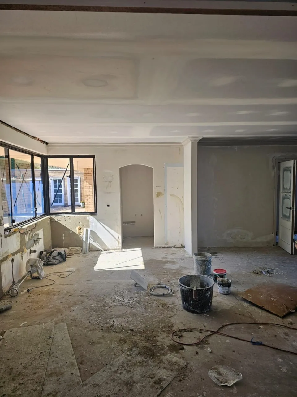 The same Roleystone lounge from the same side of the room, with a new flat ceiling set on steel furring channel, the arched opening and window bank unchanged below it